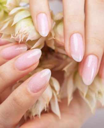 Women's hands with a beautiful pale pink manicure. The girl is holding a white flower. Professional hand care in a beauty salon.